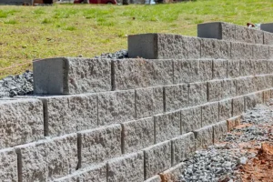 Concrete retaining wall built on a sloped yard with gravel base and level string lines, showing proper construction and drainage preparation.