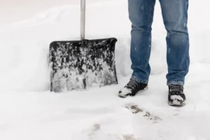 Snow plowing service clearing ice and packed snow from a driveway in Omaha, NE using a shovel during winter storm conditions