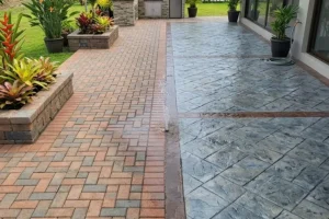 Paver patio vs stamped concrete patio comparison showing brick pavers and textured stamped concrete outdoor surfaces in residential backyard landscaping Omaha